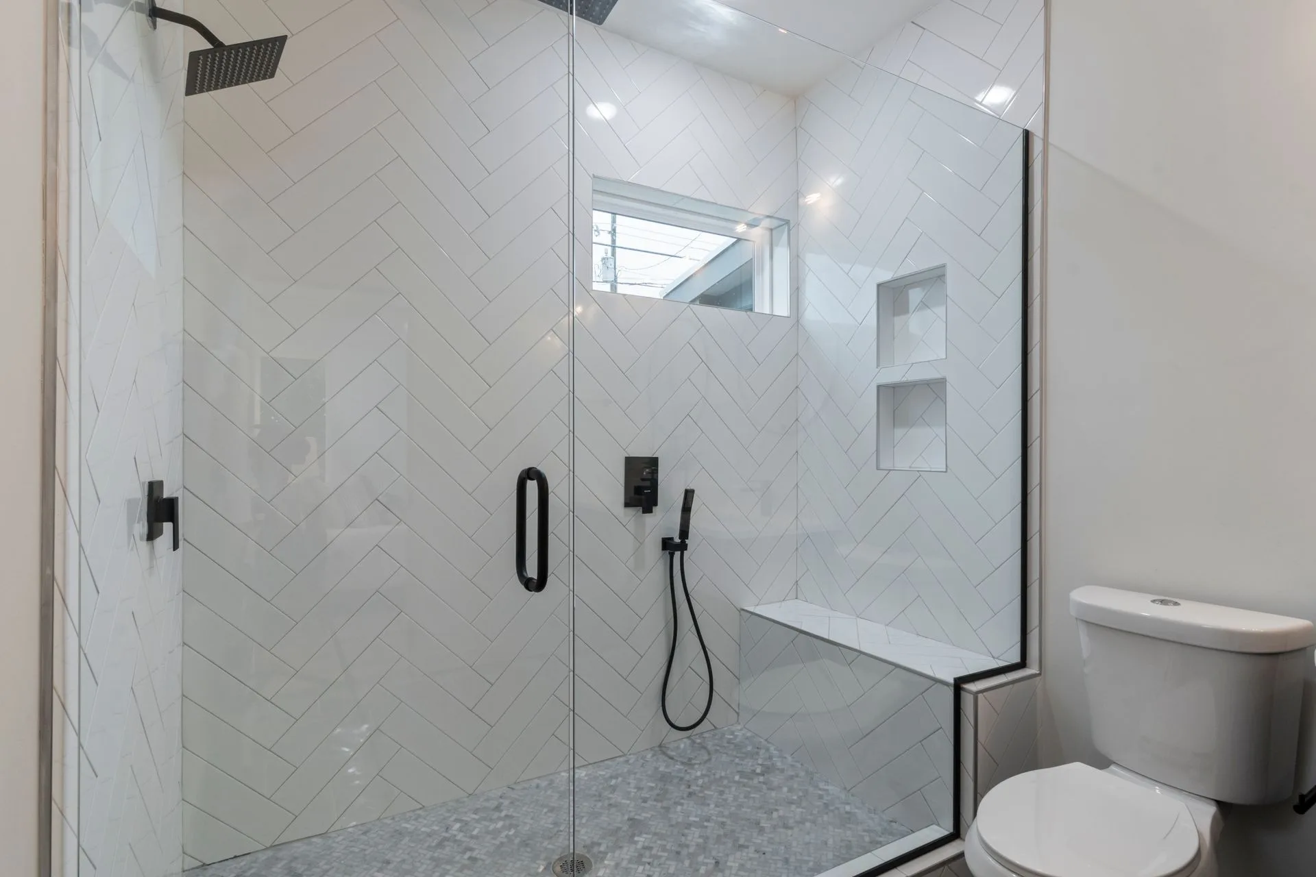 Walk-in shower with glass door, bench, and herringbone tile