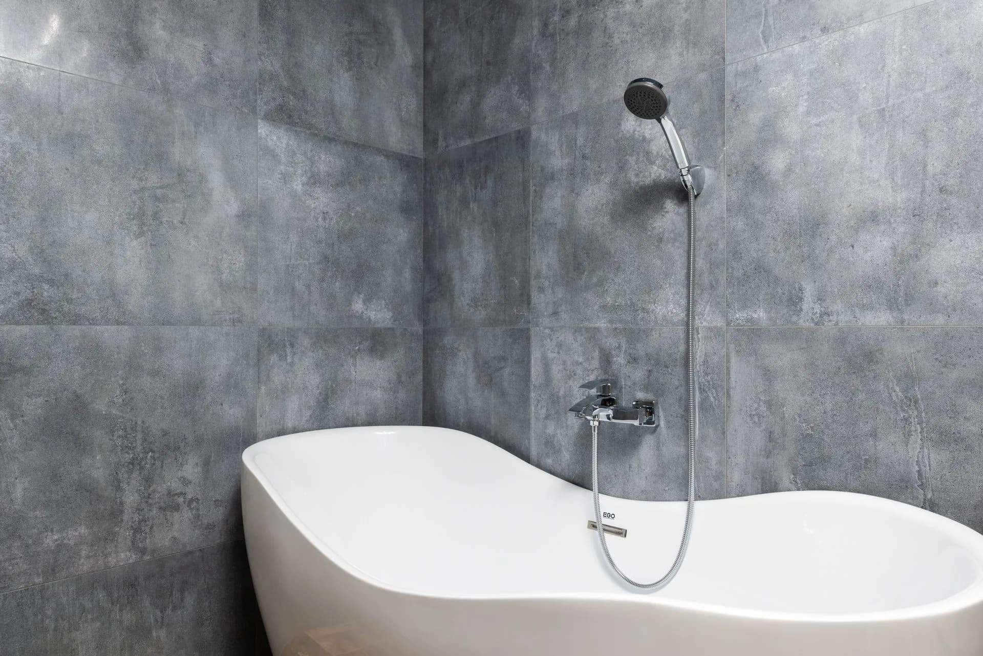 White bathtub with overhead shower on gray tiled walls